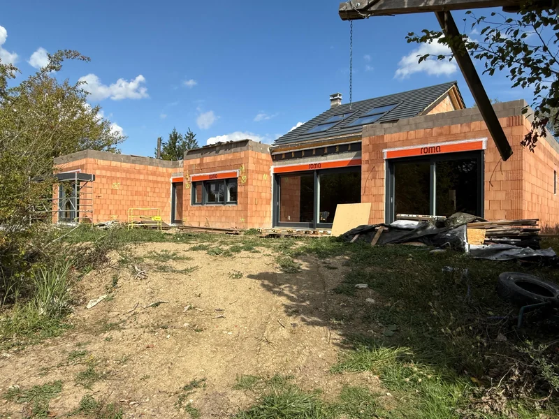 Gesamtansicht des Neubaus mit anthrazitgrauen Holzfenstern, Schiebeelementen und Aufsatzrollläden im Rohbau