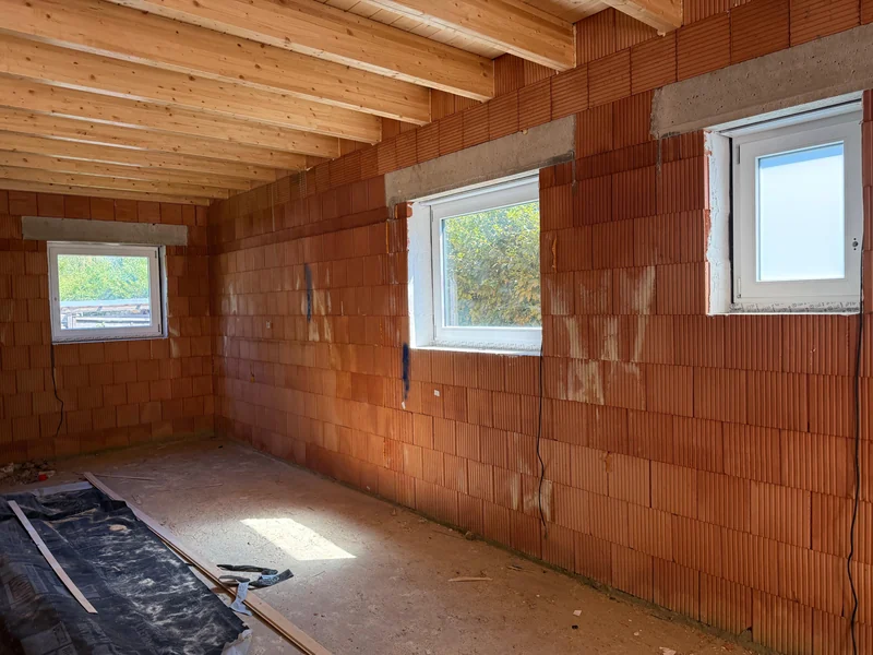 Innenansicht der weiß lackierten Holzfenster im Rohbau unter einer sichtbaren Holzbalkendecke