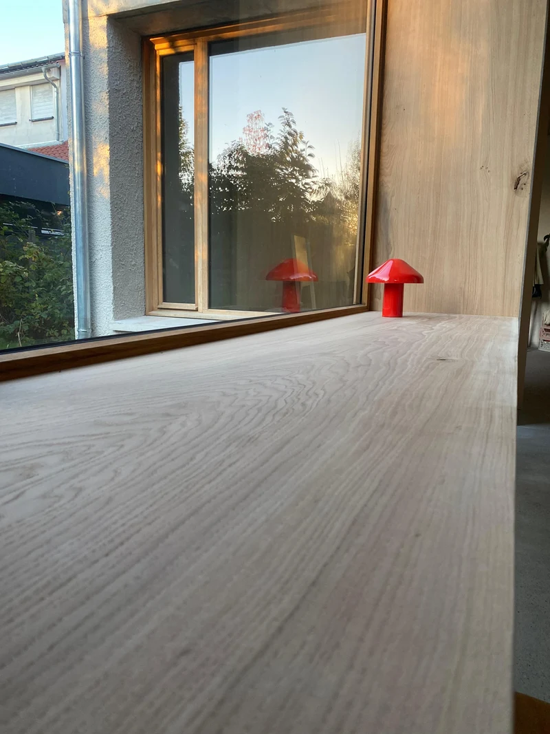 Detail der Holzoberfläche des Schreibtischs mit sichtbarer Maserung und roter Tischleuchte am Fenster