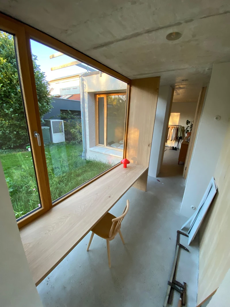 Langer Schreibtisch aus Holz an der Fensterfront mit Blick ins Grüne während der Ausbauphase