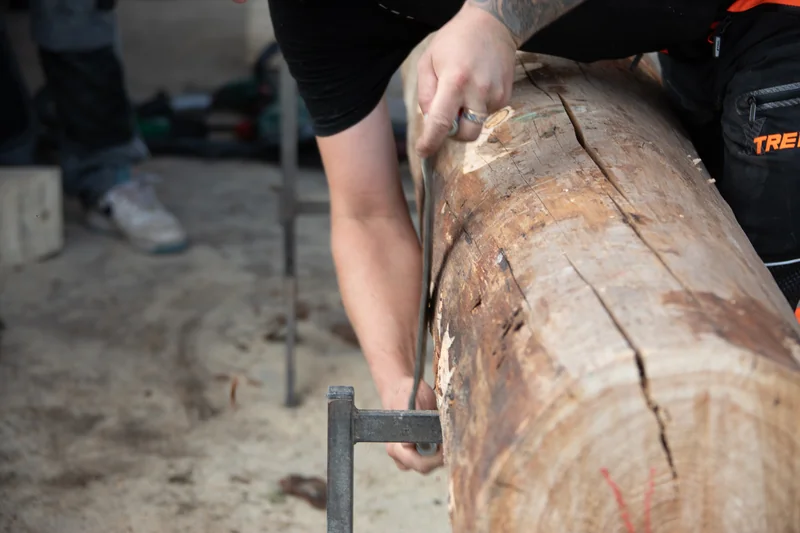 Hände bei der Bearbeitung eines eingespannten Holzstamms